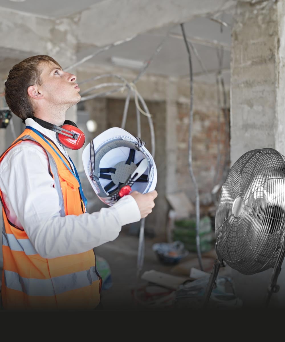 Bauarbeiter mit Schutzhelm überprüft Lüfter auf Baustelle