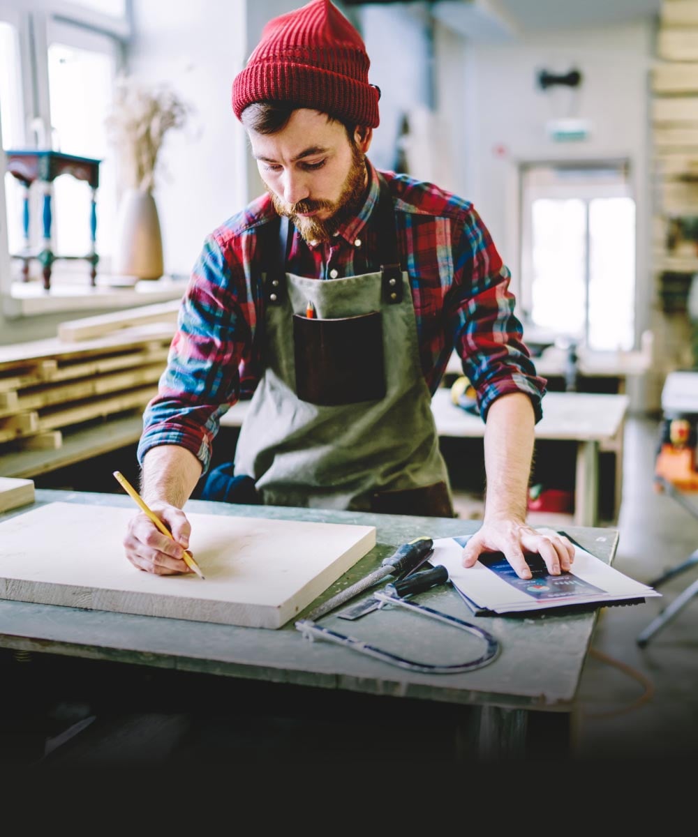Handwerker zeichnet auf Holzplatte in einer Werkstatt