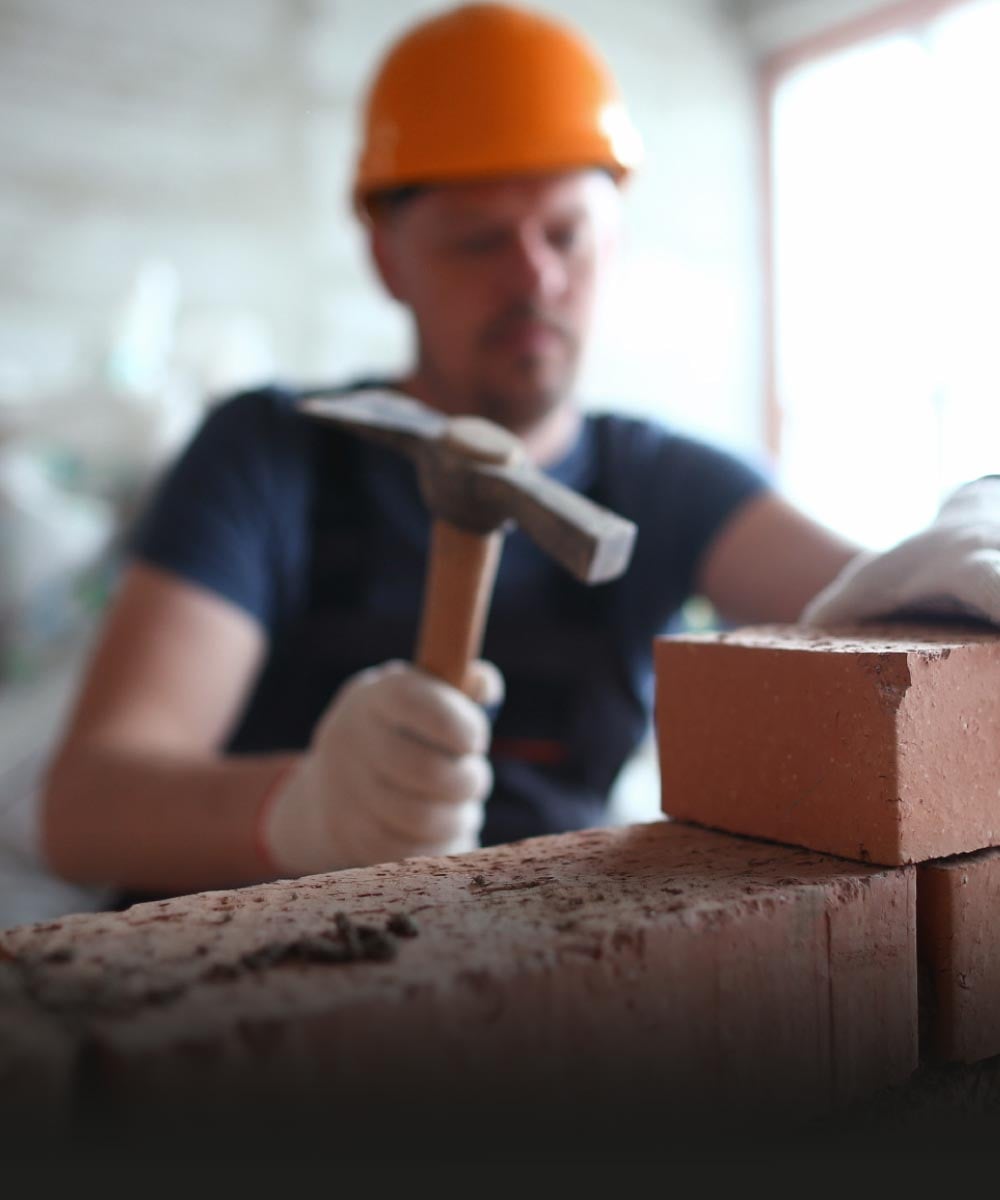 Handwerker mit Helm und Handschuhen baut eine Mauer mit Ziegeln