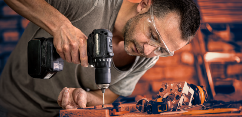 Handwerker mit Bohrmaschine arbeitet an Holzprojekt mit Schutzbrille und hochwertigem Werkzeug