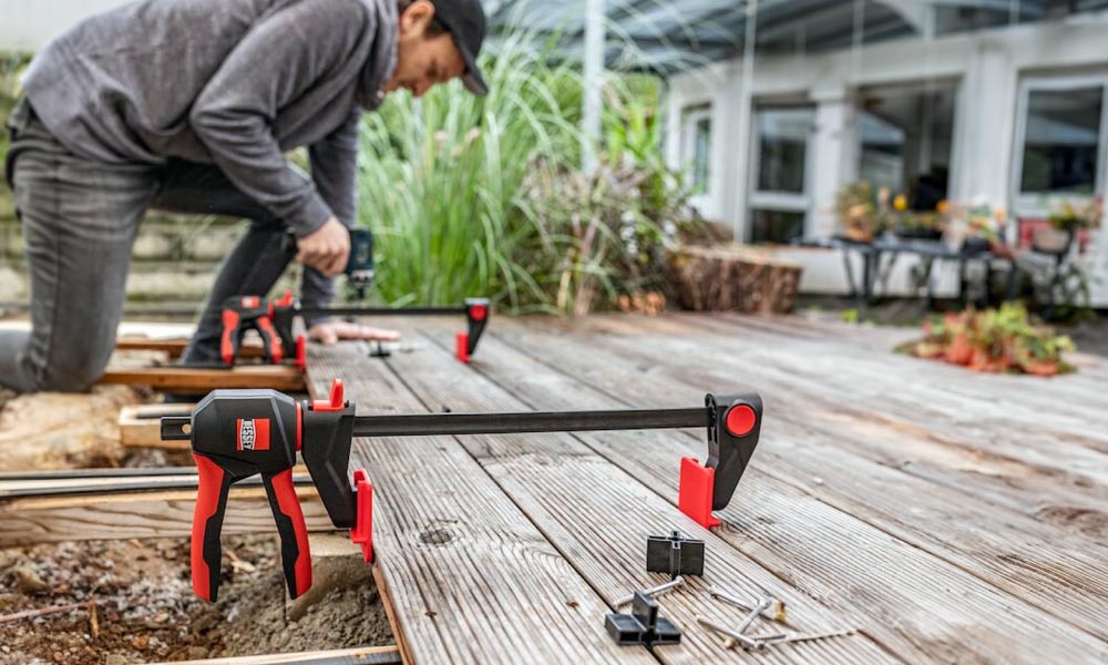 Bessey Einhandzwinge für präzise Arbeiten bei der Terrassendielenmontage Bessey Einhandzwinge bei der Verlegung von Terrassendielen im Außenbereich