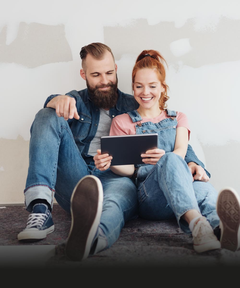 Junges Paar im Casual-Look sitzt auf dem Boden und schaut auf ein Tablet