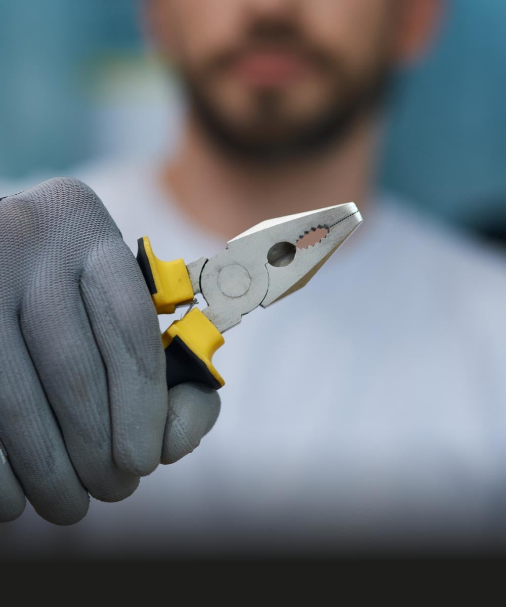 Hand hält Zange mit grauen Arbeitshandschuhen