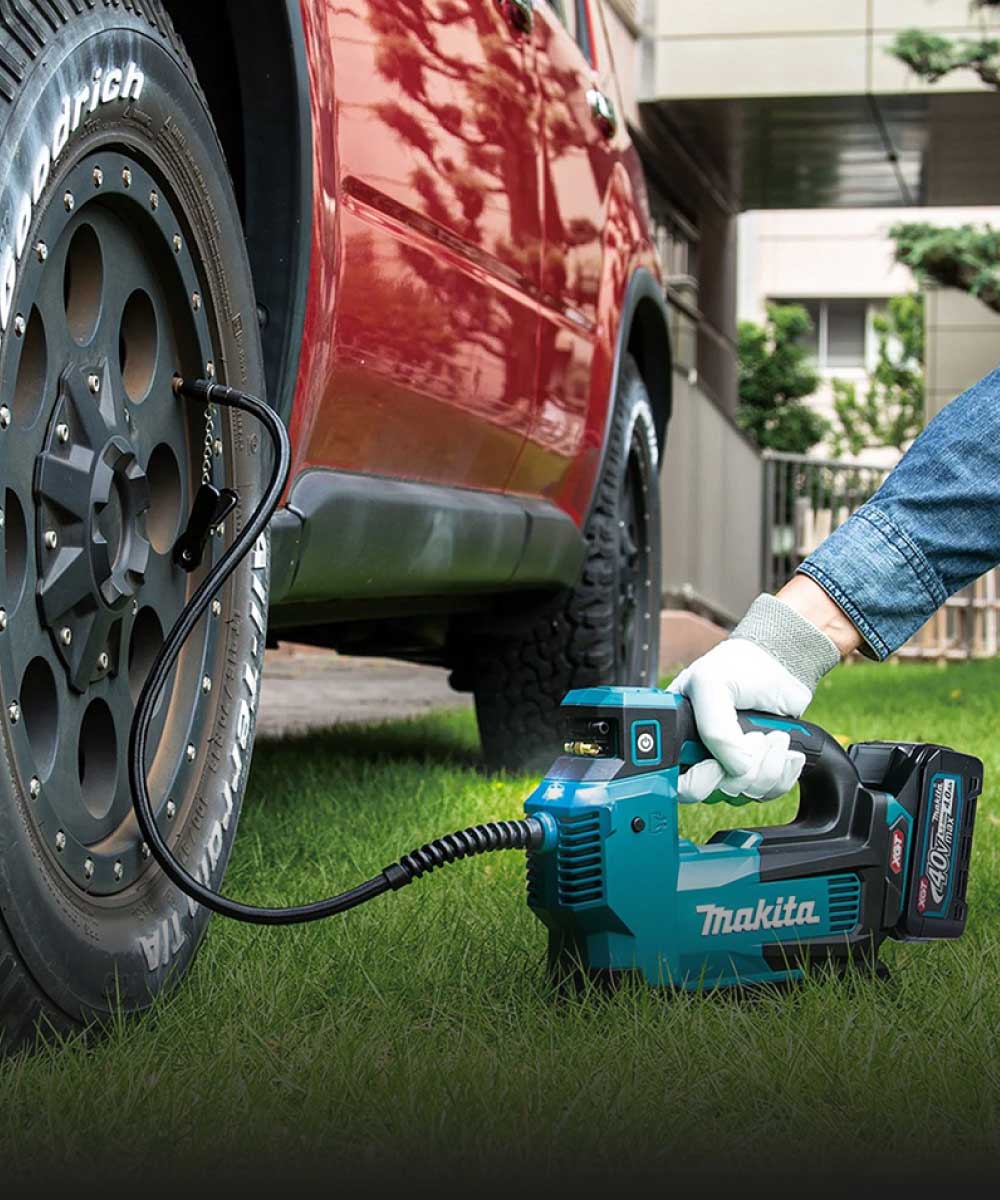 Arbeiter nutzt Makita Luftkompressor für Autoreifen auf grünem Rasen