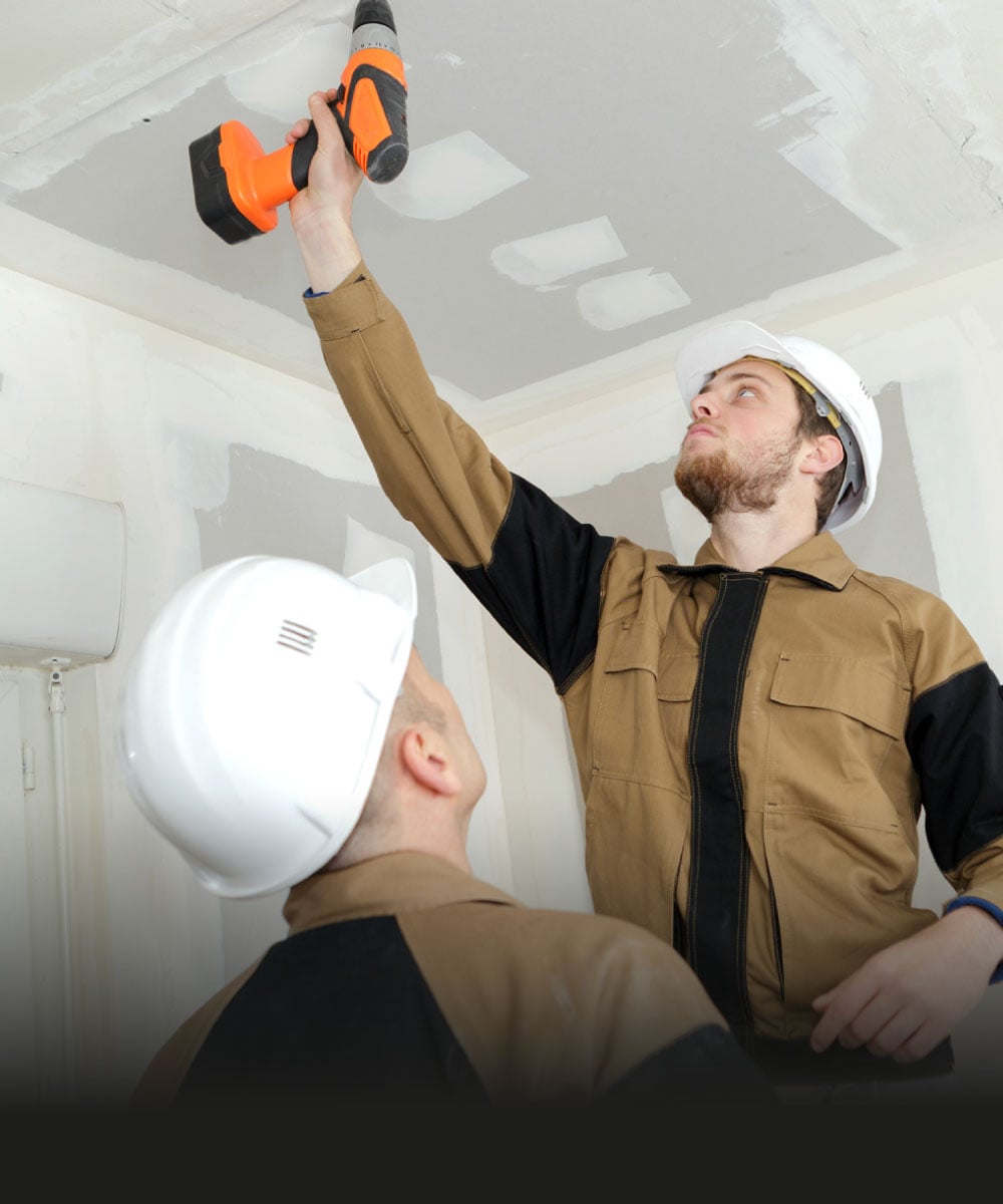 Zwei Handwerker mit Sicherheitshelmen und Bohrmaschine an der Decke