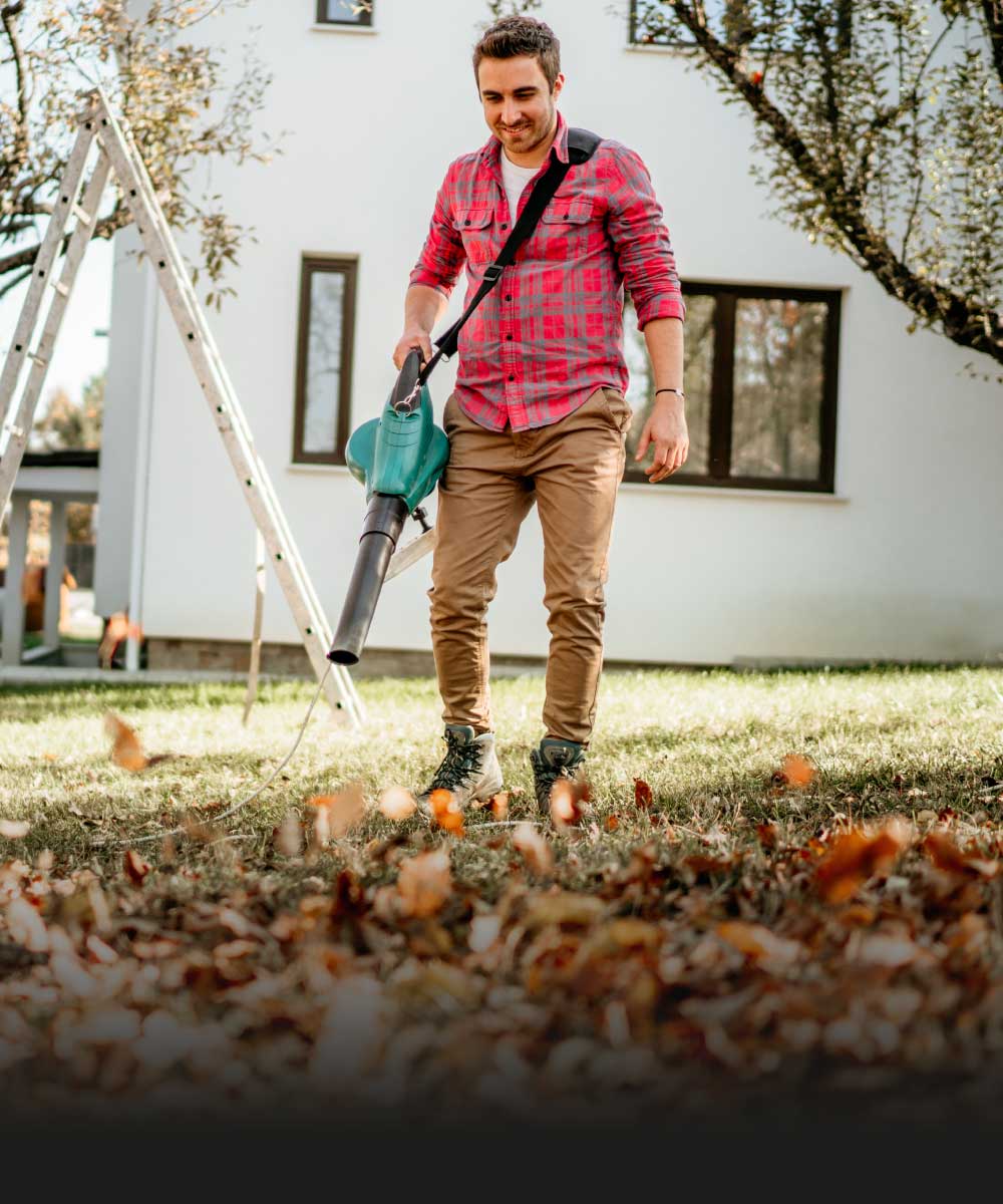 Mann verwendet Laubbläser im Garten zur Reinigung von Herbstlaub