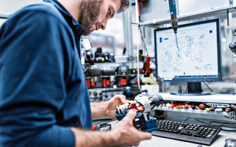 Techniker überprüft Akkugerät mit technischer Zeichnung im Hintergrund